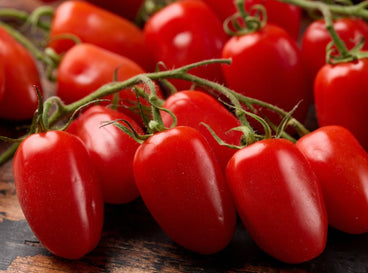 A close-up shot of several elongated, red fruits, placed on top of a wooden surface, showcasing sweet tomatoes