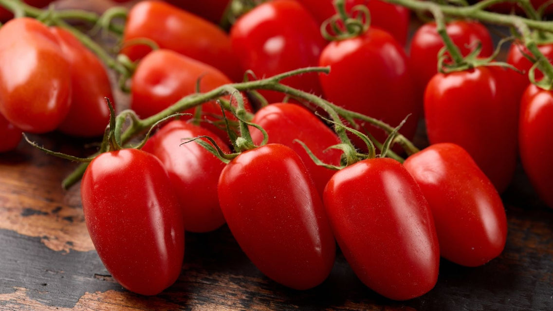 A close-up shot of several elongated, red fruits, placed on top of a wooden surface, showcasing sweet tomatoes
