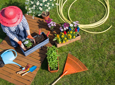 An overhead shot of a person in the process of tending to planters alongside several garden tools, showcasing june gardening tasks