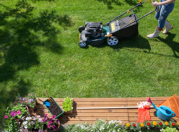 A shot of a person mowing a lawn area alongside several garden tools for spring clean up
