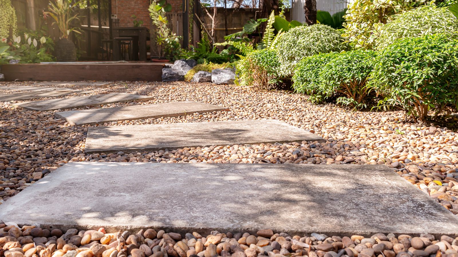 A gravel pathway in a garden with plants on the edges and large rock slabs forming the path