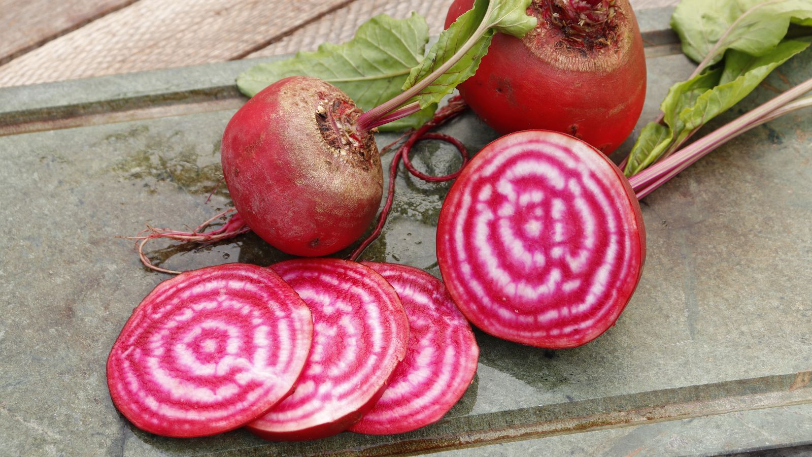 An overhead and close-up shot of freshly harvested Chioggia Beets, showcasing its striped interiors, all placed in a stone surface indoors